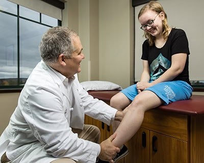 A doctor examining a teenage girl's leg during a consultation in a medical office setting.