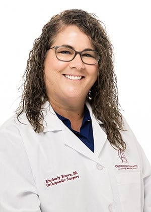 A smiling female orthodontist wearing glasses and a white medical coat, representing expert orthodontic care and dental health services.