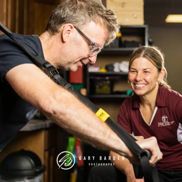 Assisted patient undergoing physical therapy with an orthopedic strap, guided by a smiling specialist in a clinical setting.