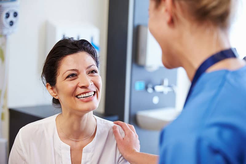 An accessible image showing a healthcare professional providing comfort to a smiling female patient in a clinical setting, emphasizing compassionate medical care and patient support.