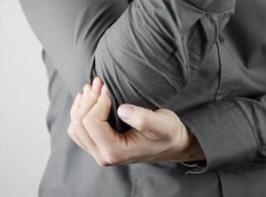 A person wearing a gray long-sleeve shirt holding their elbow, indicating arm pain or discomfort, ideal for topics on sports injuries, elbow pain relief, or health tips.